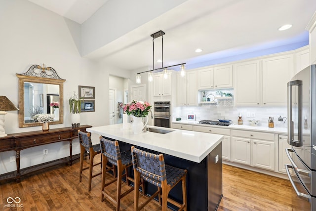 kitchen featuring a kitchen bar, a center island with sink, stainless steel appliances, light wood finished floors, and decorative backsplash