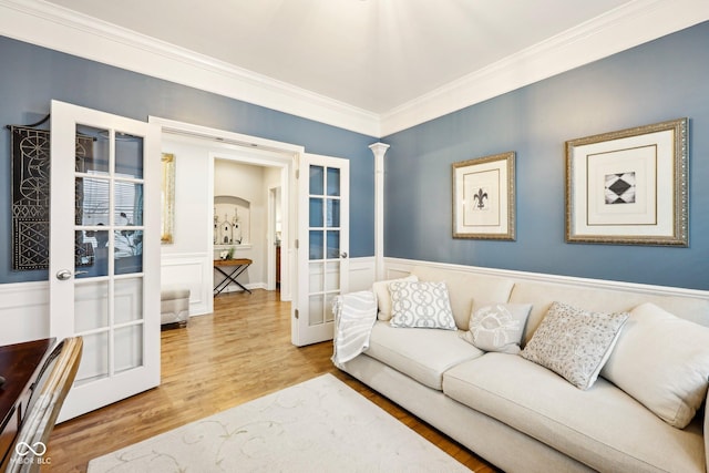 living area with a wainscoted wall, ornamental molding, french doors, wood finished floors, and ornate columns