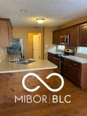 kitchen with appliances with stainless steel finishes, a peninsula, light countertops, and a sink