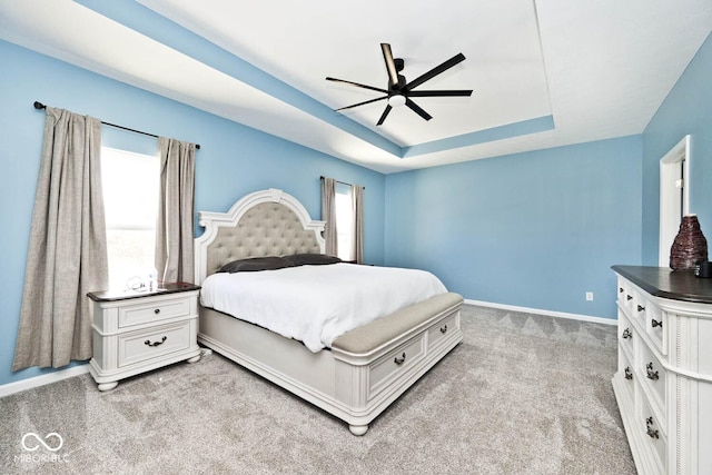 bedroom featuring a ceiling fan, a tray ceiling, light colored carpet, and baseboards