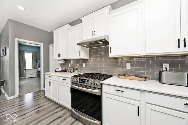 kitchen featuring white cabinets, stainless steel range with gas stovetop, light countertops, under cabinet range hood, and backsplash