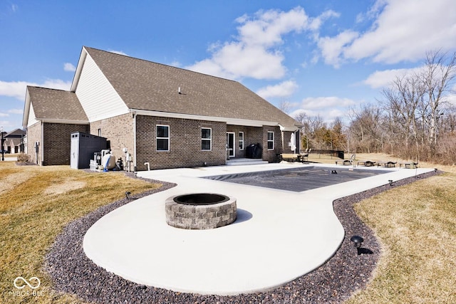 back of property featuring roof with shingles, brick siding, a patio, a lawn, and an outdoor fire pit