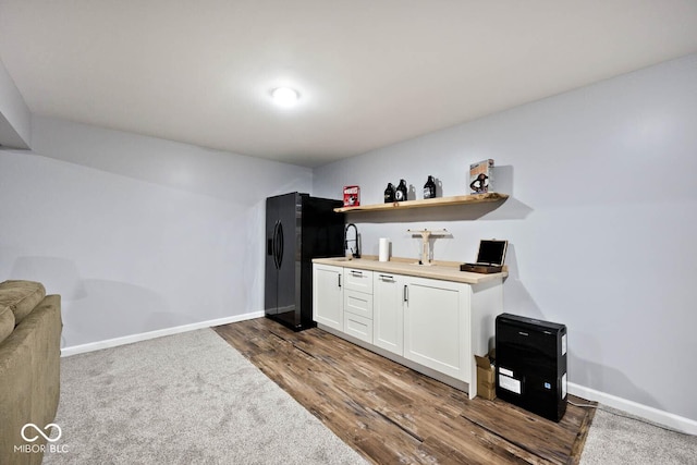 kitchen featuring baseboards, dark wood-type flooring, black refrigerator with ice dispenser, light countertops, and white cabinetry