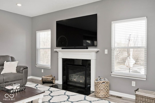 living room featuring a fireplace with flush hearth, visible vents, baseboards, and wood finished floors