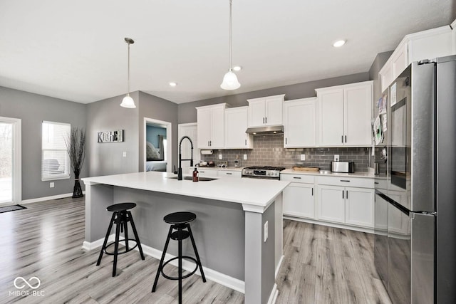 kitchen featuring stainless steel appliances, backsplash, light wood-style flooring, and under cabinet range hood