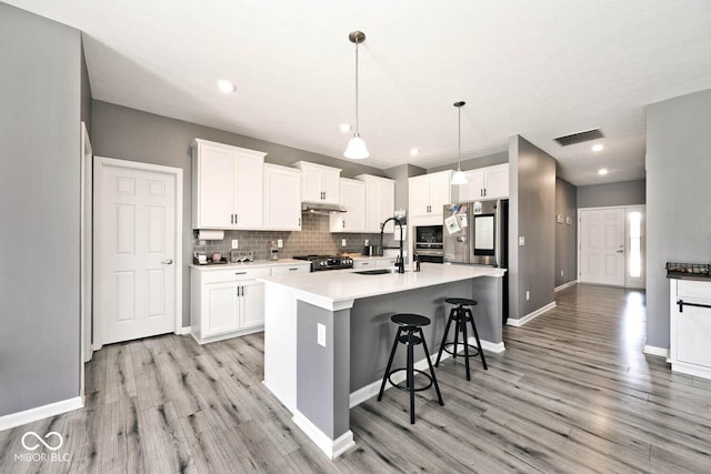 kitchen with tasteful backsplash, light wood-style flooring, a sink, under cabinet range hood, and a kitchen breakfast bar