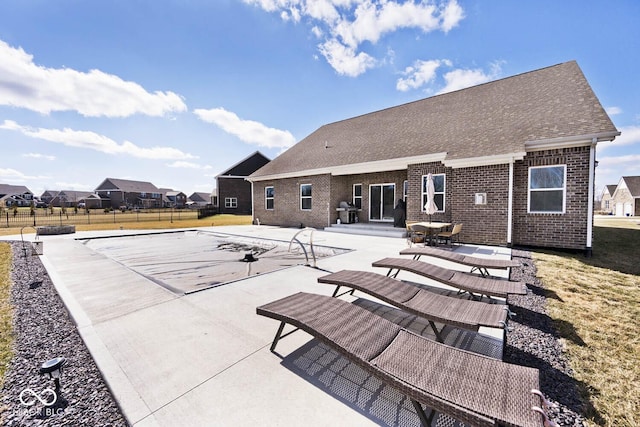 rear view of property with brick siding, a shingled roof, fence, and a patio