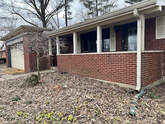 view of side of home with covered porch, brick siding, and an attached garage