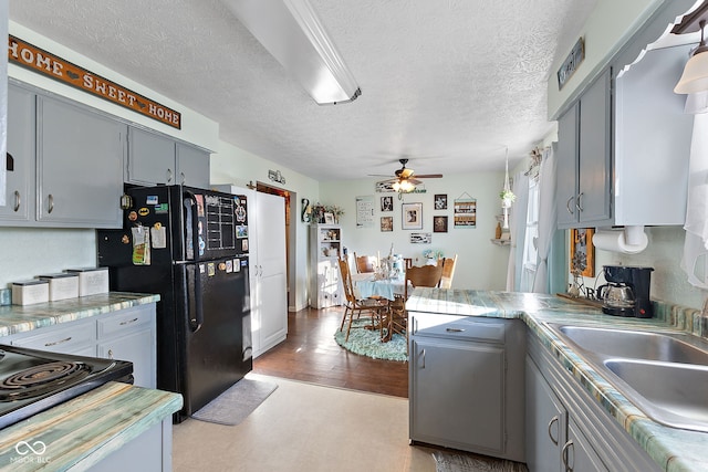 kitchen featuring a peninsula, a sink, light countertops, gray cabinets, and freestanding refrigerator