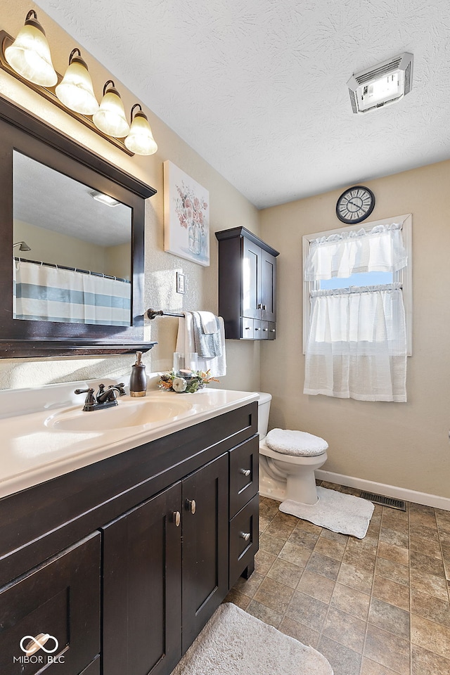 bathroom featuring baseboards, toilet, vanity, and a textured ceiling