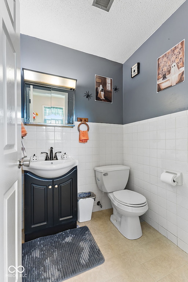 half bath with tile walls, toilet, wainscoting, a textured ceiling, and vanity