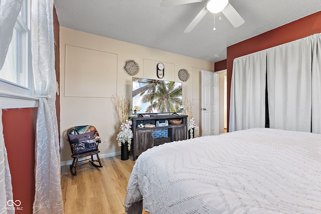 bedroom with a ceiling fan, a textured ceiling, baseboards, and wood finished floors