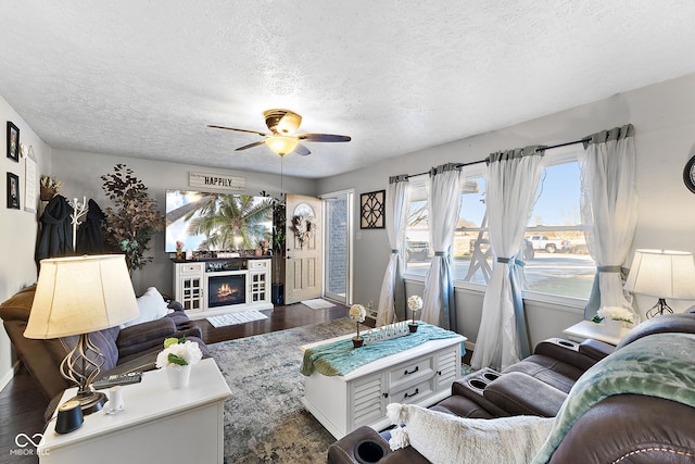 living room featuring a textured ceiling, a ceiling fan, wood finished floors, and a glass covered fireplace