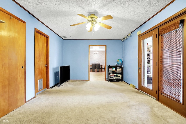 interior space with a textured ceiling, a ceiling fan, crown molding, and light colored carpet