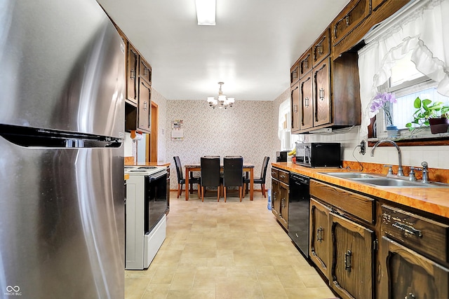 kitchen with a chandelier, a sink, wooden counters, black appliances, and wallpapered walls