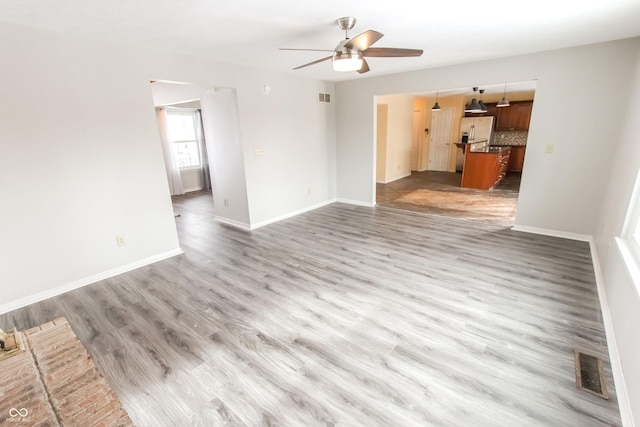 unfurnished living room featuring a ceiling fan, visible vents, baseboards, and wood finished floors