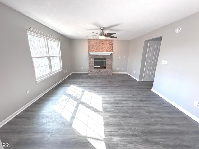 unfurnished living room with ceiling fan, dark wood-style flooring, a brick fireplace, and baseboards