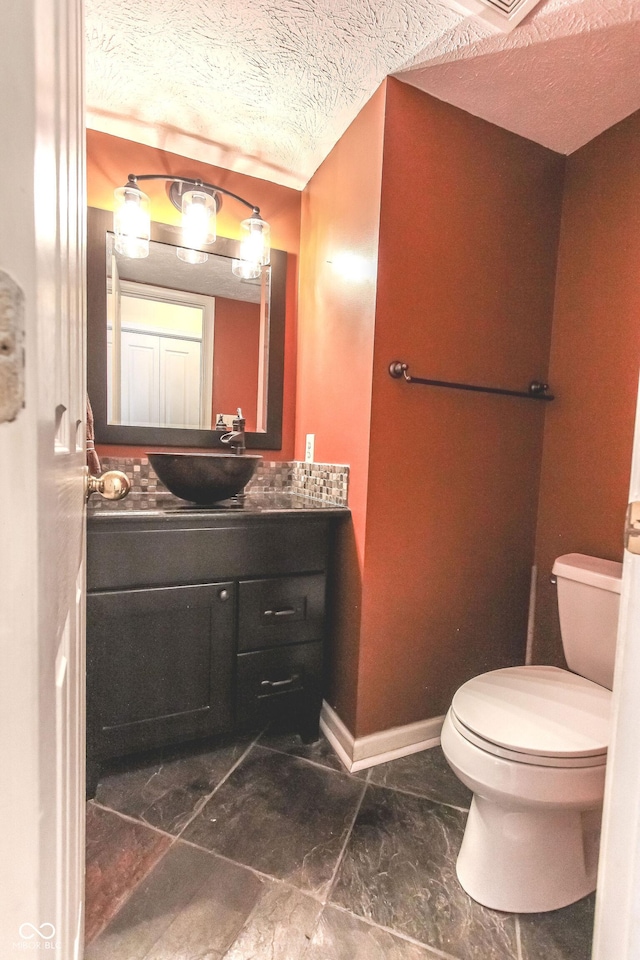 bathroom with toilet, a textured ceiling, baseboards, and vanity