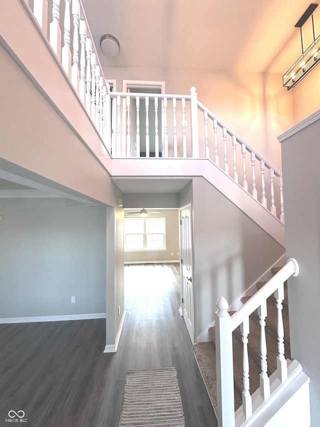 stairway featuring a towering ceiling, baseboards, and wood finished floors