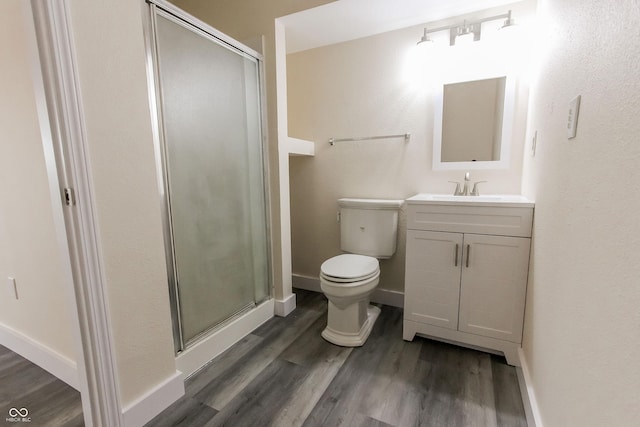 full bathroom featuring toilet, wood finished floors, vanity, baseboards, and a stall shower