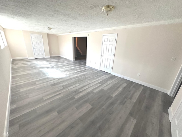 unfurnished bedroom with baseboards, dark wood finished floors, ornamental molding, a textured ceiling, and multiple closets