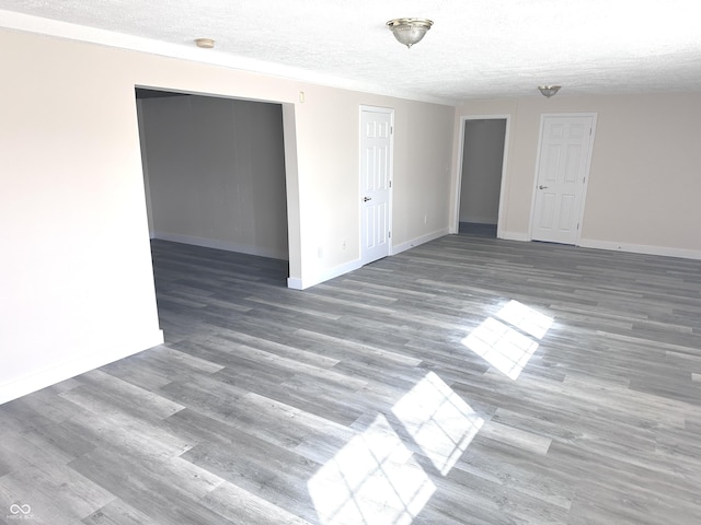 empty room featuring a textured ceiling, wood finished floors, and baseboards