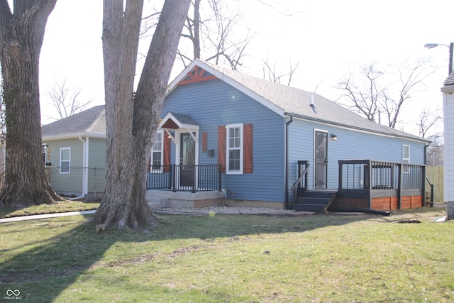 view of front of house with a deck, a front yard, and roof with shingles