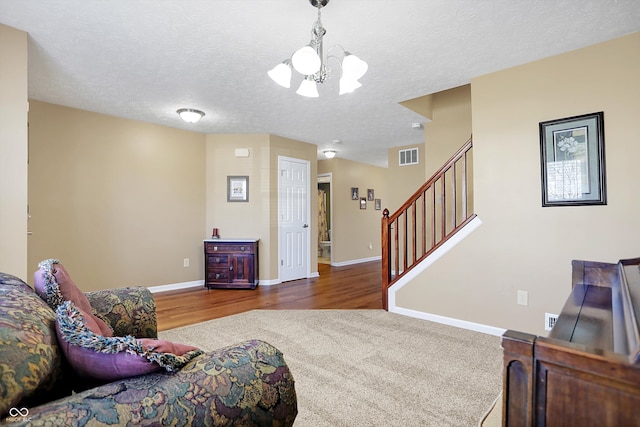 carpeted living area featuring visible vents, a textured ceiling, baseboards, a chandelier, and stairs