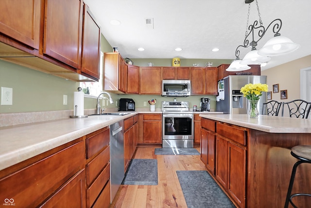 kitchen featuring light wood-type flooring, pendant lighting, a sink, appliances with stainless steel finishes, and light countertops