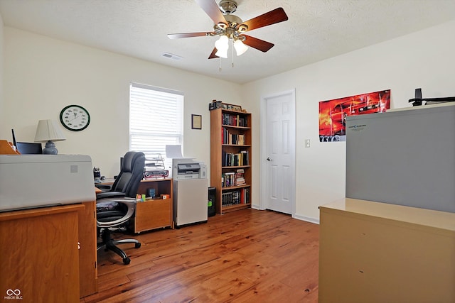 office area featuring visible vents, a textured ceiling, light wood-type flooring, and a ceiling fan