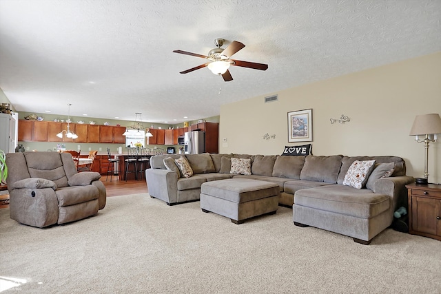 living room featuring a textured ceiling, light colored carpet, visible vents, and ceiling fan