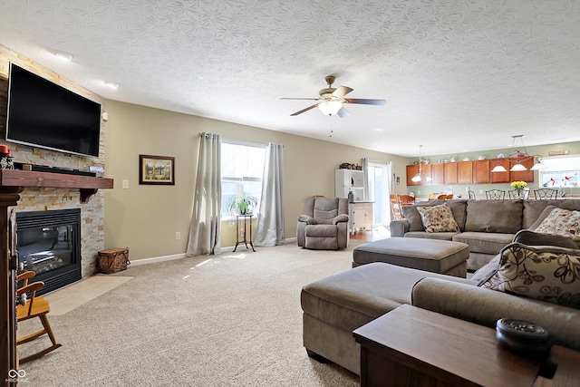 living area featuring a ceiling fan, baseboards, a fireplace, a textured ceiling, and light carpet