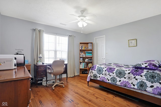 bedroom with baseboards, visible vents, light wood-style flooring, ceiling fan, and a textured ceiling