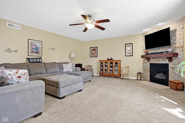 carpeted living room with a textured ceiling, a stone fireplace, visible vents, and ceiling fan