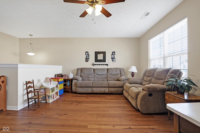 living room with visible vents, baseboards, light wood-style floors, a textured ceiling, and a ceiling fan