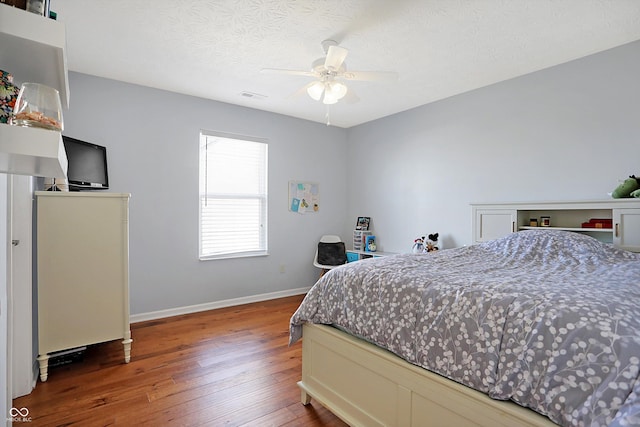 bedroom with visible vents, a textured ceiling, wood-type flooring, baseboards, and ceiling fan