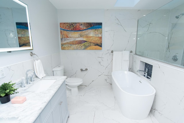 bathroom with marble finish floor, toilet, vanity, a freestanding tub, and stone wall