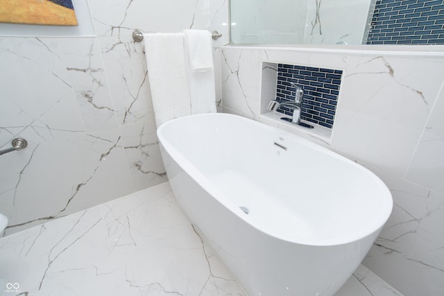 full bathroom featuring stone wall, marble finish floor, and a freestanding tub