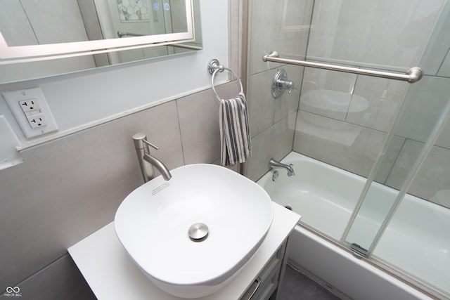 full bathroom featuring tile walls, bath / shower combo with glass door, and a sink