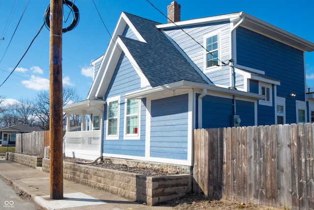 view of property exterior featuring covered porch, roof with shingles, fence, and a chimney