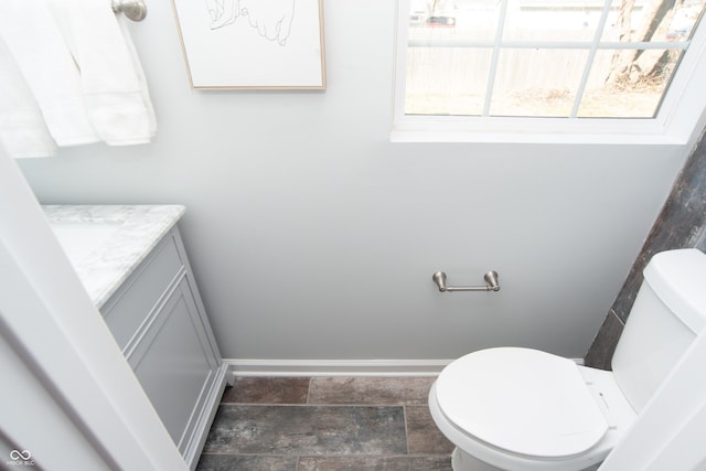 half bathroom with toilet, stone finish flooring, vanity, and baseboards