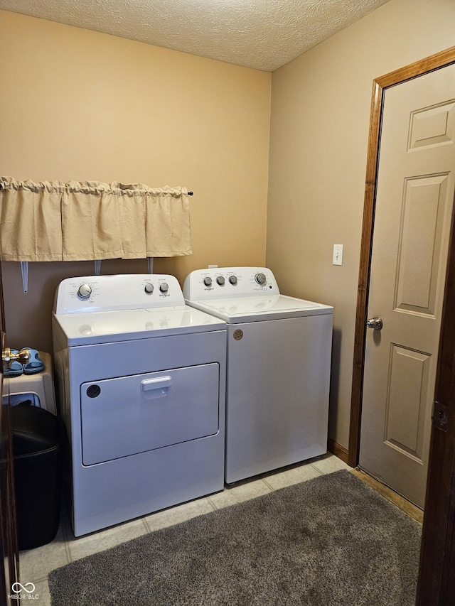 washroom featuring light tile patterned floors, laundry area, a textured ceiling, and washing machine and clothes dryer