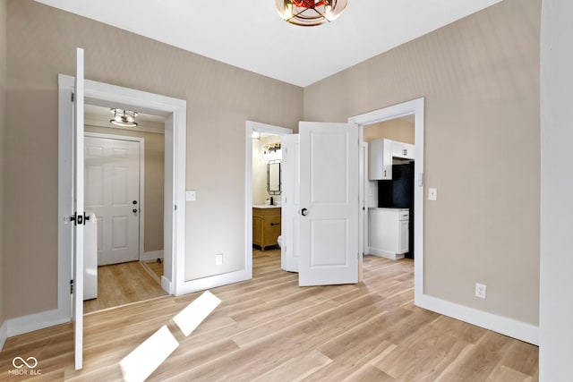 unfurnished bedroom with baseboards, ensuite bathroom, and light wood-style floors