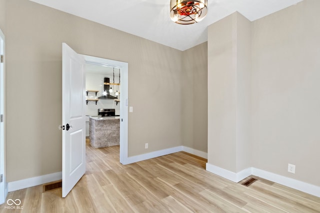 unfurnished room featuring visible vents, an inviting chandelier, light wood-type flooring, and baseboards