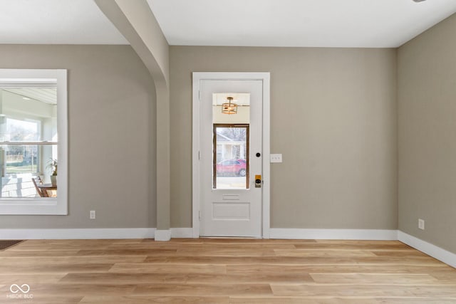 foyer entrance featuring arched walkways, plenty of natural light, and light wood-style floors