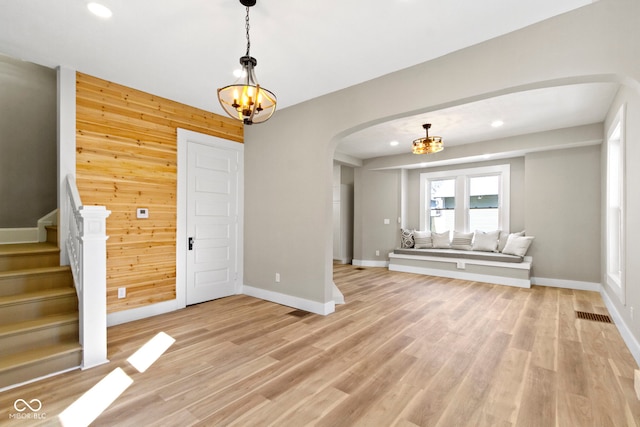 foyer entrance with wooden walls, light wood-style flooring, arched walkways, stairs, and a notable chandelier