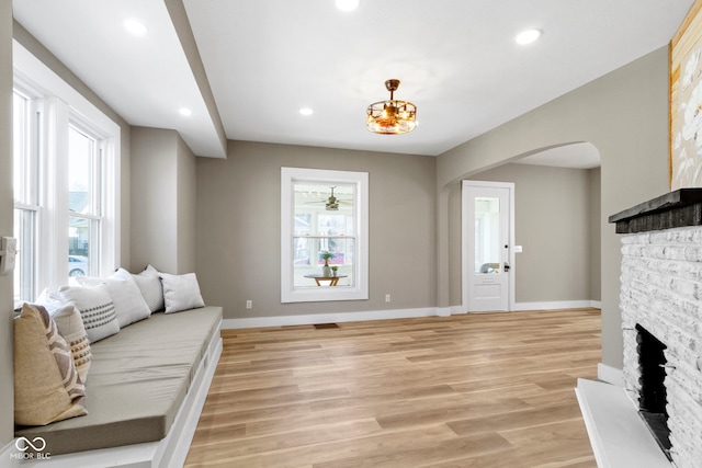 living room with recessed lighting, arched walkways, a stone fireplace, light wood finished floors, and baseboards