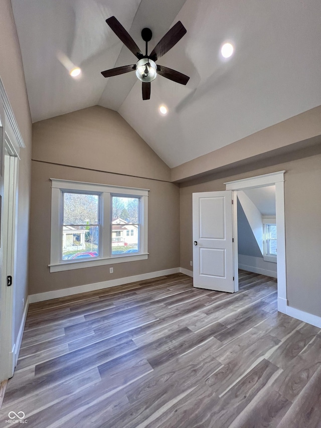 unfurnished bedroom featuring baseboards, multiple windows, wood finished floors, and vaulted ceiling