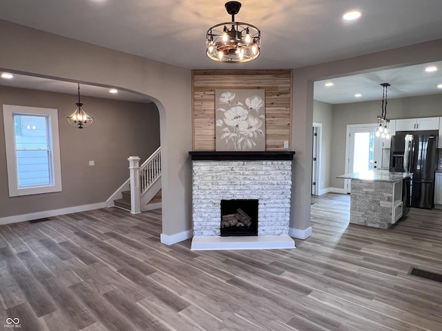 unfurnished living room featuring a stone fireplace, wood finished floors, and a chandelier