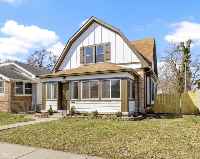 view of front facade featuring board and batten siding, a shingled roof, a front yard, and fence